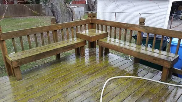 Wooden corner bench deck with green algae on the boards, mid-wash, a hose across the planks