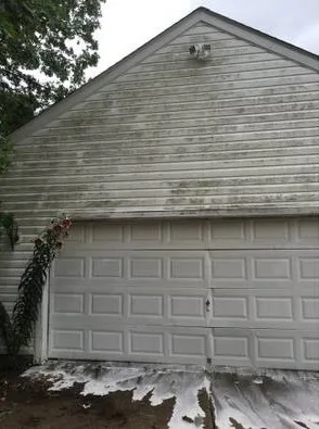 Vinyl-sided garage gable streaked green with mildew, a stained slab below