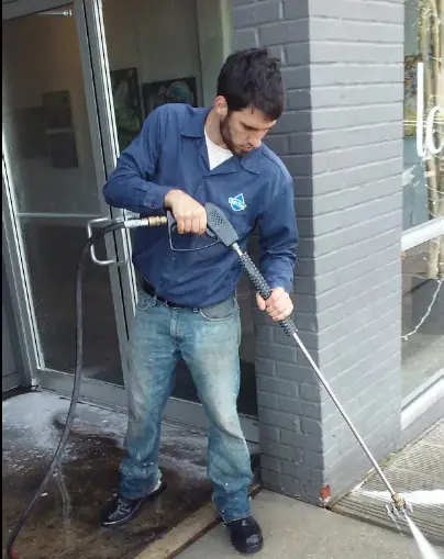 Technician in a blue Tiger Wash work shirt washing a storefront entry with a wand